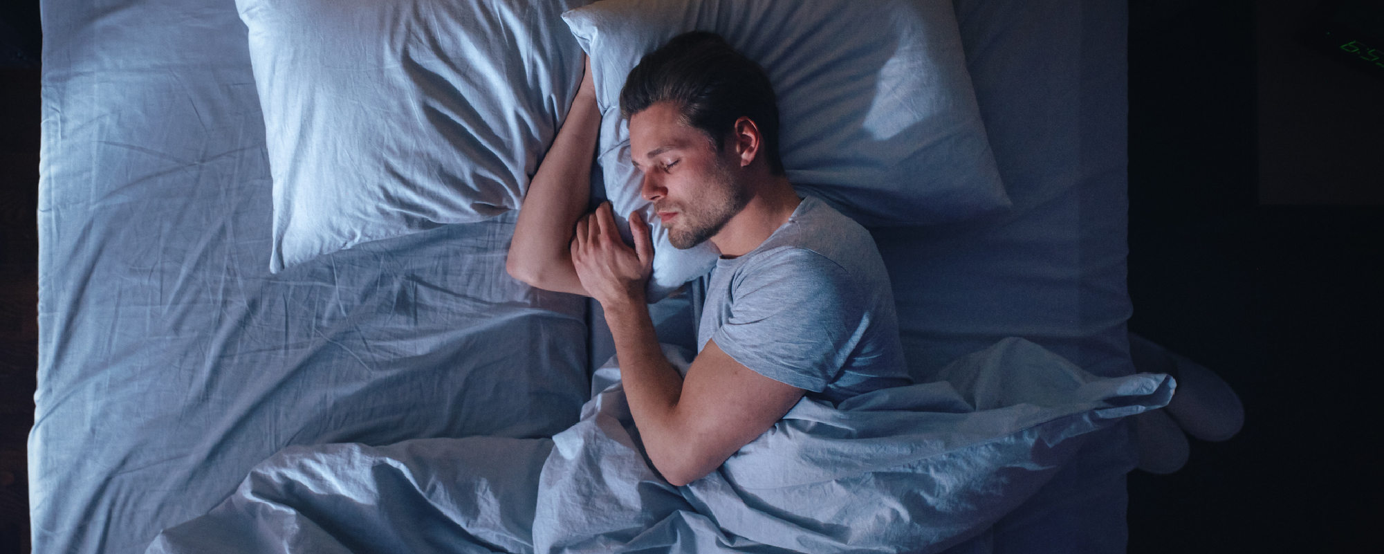Man sleeping peacefully on his side in bed under blue-gray sheets.